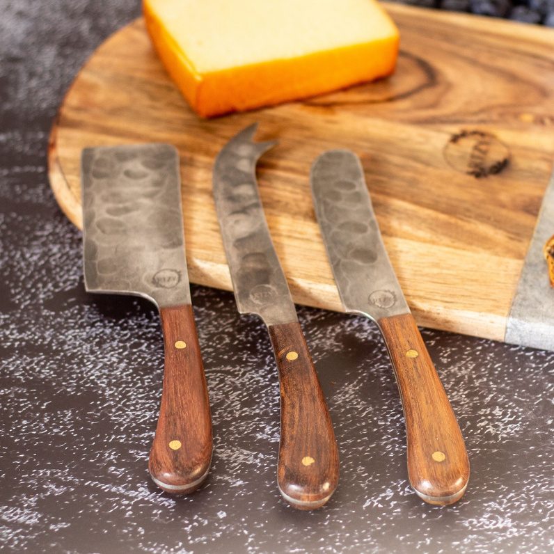 Hammered cheese knives on a wooden board with cheese